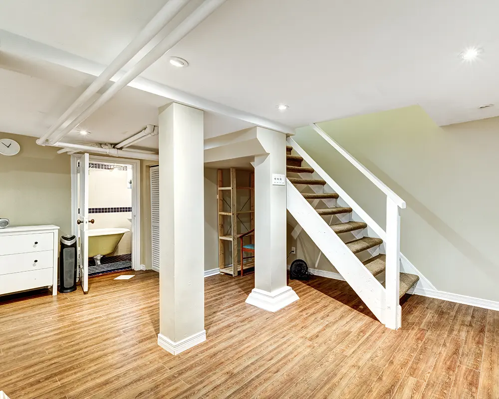 "Basement revealing an expansive open space with visible stairs leading upward and a bathroom tucked in the back. Versatile layout with minimalist design elements. Ample room for various configurations, offering flexibility and functionality.