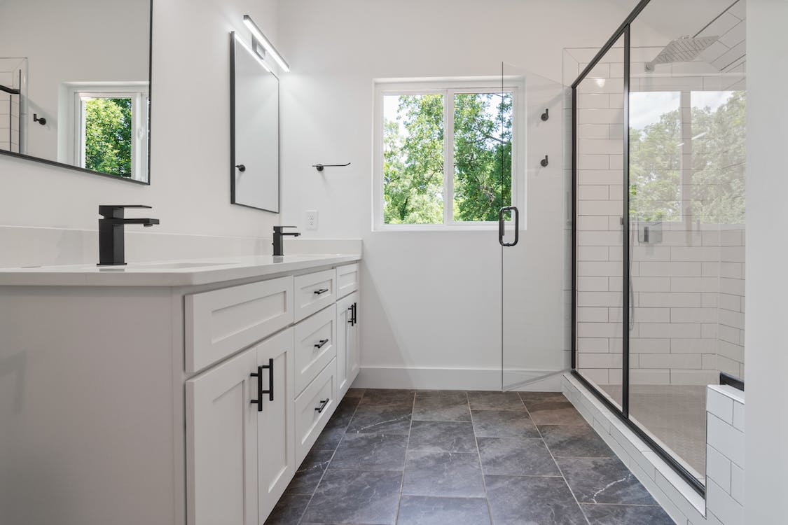 Compact white-themed bathroom featuring a sleek modern design, with minimalist fixtures and a space-saving layout. The bathroom showcases a clean, crisp aesthetic with white tiles, double sink, a mirror, and subtle lighting, maximizing functionality in a limited space.