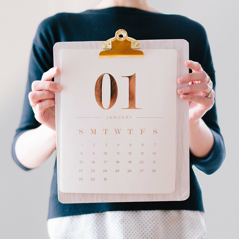 A person holding up a clipboard with a monthly calendar.