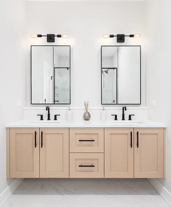 White bathroom with wood cabinets, two white sinks with black faucets and two mirrors.
