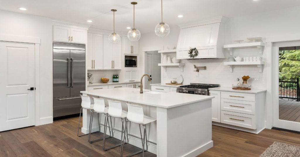 Modern white kitchen with shaker cabinets, quartz countertops, a large island with bar seating, and stainless steel appliances.