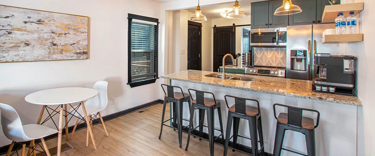 Contemporary kitchen and dining area with granite island, black barstools, and open shelving with modern decor