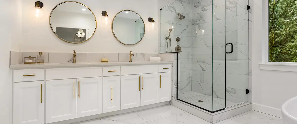 Luxury white bathroom with marble tile floor, double vanity with gold accents, and glass-enclosed rainfall shower.