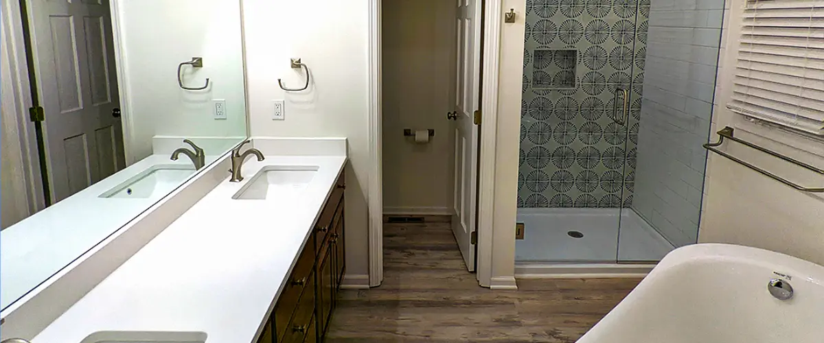 Modern bathroom remodel with double vanity, white countertops, wood cabinets, and walk-in shower with patterned tile.