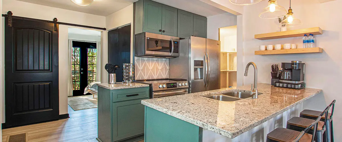 Modern kitchen with green cabinets, granite countertops, stainless steel appliances, and industrial pendant lighting