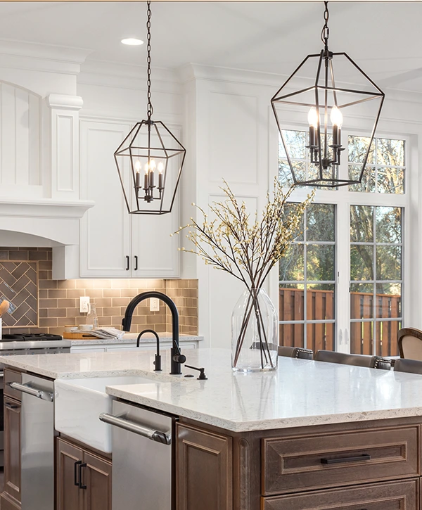 Black geometric metal pendant lights hanging above a kitchen island in a bright white kitchen.