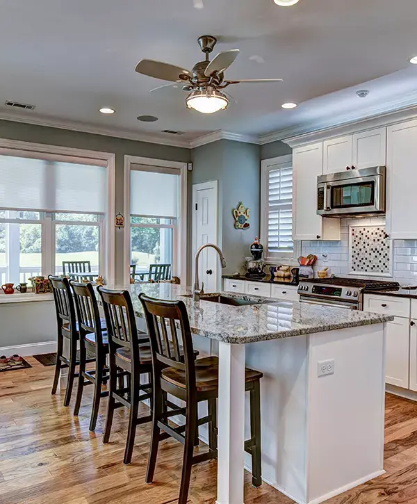 A spacious marble kitchen island with four wooden stools and a ceiling fan installed by kitchen remodeling contractors in Raytown, MO.