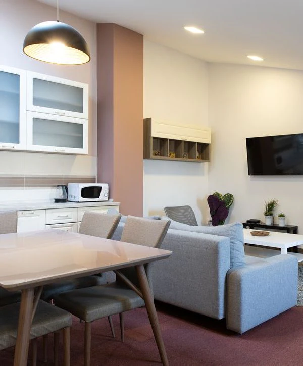 A modern basement remodeling in Leawood, KS, featuring a functional kitchenette with white cabinets, a dining table, and a cozy grey sofa in an open-concept living space.