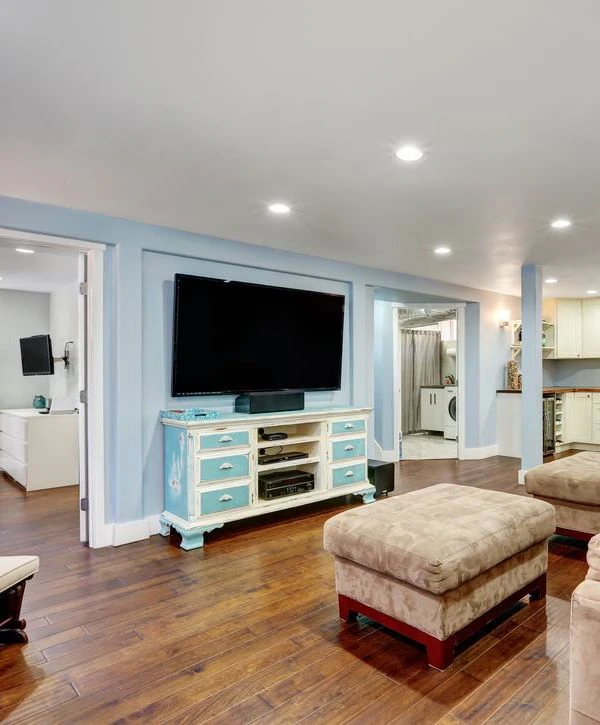 An open-concept living area with light blue walls, a large flat-screen TV on a vintage console, and hardwood floors after a complete basement remodeling in Raytown, MO.