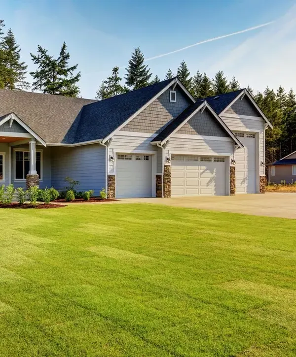 A large suburban home with gray siding, white garage doors, and a perfectly manicured green lawn by design-build remodeling companies in Raytown, MO.