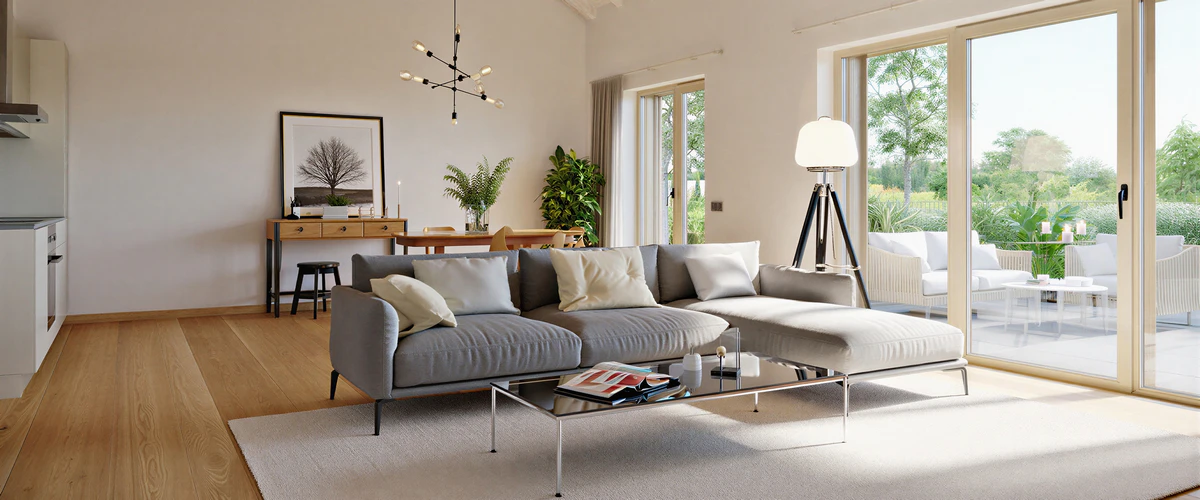 A bright, modern home living room featuring a minimal grey sectional sofa, light wood flooring, and large sliding glass doors opening to a lush outdoor patio.