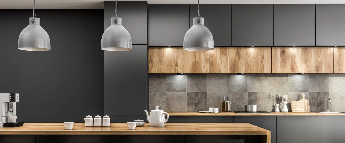 Modern dark grey kitchen showcasing matte black cabinets, warm wood countertops and lower backsplash, industrial concrete dome pendant lights, and a white tea set on the counter.