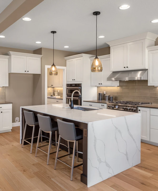Spacious kitchen refresh in Leawood, KS featuring white cabinetry, wood floors, a large island with a waterfall marble edge, grey bar stools, and warm glass pendant lighting.